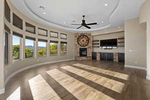 Unfurnished living room with a raised ceiling, recessed lighting, a ceiling fan, light wood finished floors, and a stone fireplace