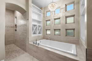 Bathroom featuring a garden tub, healthy amount of natural light, a tile shower, a towering ceiling, and tile patterned flooring