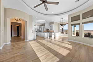 Unfurnished living room featuring a tray ceiling, ceiling fan, light wood-style flooring, arched walkways, and recessed lighting