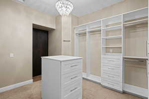Walk in closet featuring a chandelier and light carpet