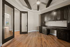 Unfurnished office with built in study area, dark wood-style floors, beamed ceiling, and ceiling fan