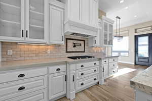Kitchen featuring glass insert cabinets, white cabinetry, light stone countertops, decorative backsplash, and decorative light fixtures