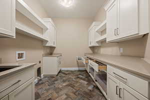 Laundry area with dark stone finish floors, hookup for a washing machine, electric dryer hookup, and cabinet space