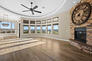 Unfurnished living room with a tray ceiling, wood finished floors, a fireplace, recessed lighting, and ceiling fan