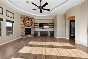 Unfurnished living room with wood finished floors, a tray ceiling, a ceiling fan, arched walkways, and recessed lighting