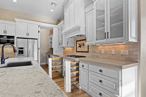 Kitchen featuring white cabinetry, decorative backsplash, light stone counters, glass insert cabinets, and recessed lighting