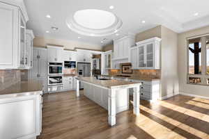 Kitchen featuring glass insert cabinets, a tray ceiling, decorative backsplash, a breakfast bar, and recessed lighting