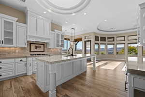 Kitchen with a tray ceiling, glass insert cabinets, white cabinetry, pendant lighting, and recessed lighting