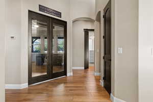 Entrance foyer featuring arched walkways, light wood finished floors, and french doors
