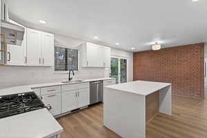 Kitchen with brick wall, light stone counters, white cabinetry, appliances with stainless steel finishes, and recessed lighting