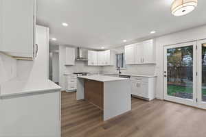 Kitchen featuring a kitchen island, white cabinetry, light stone countertops, wall chimney range hood, and recessed lighting