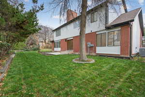 Rear view of property with brick siding, a lawn, a patio area, and a chimney