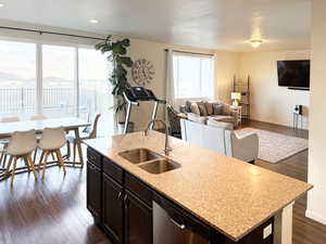 Kitchen with dark wood-style flooring, a kitchen island with sink, open floor plan, stainless steel dishwasher, and light stone counters
