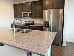 Kitchen with dark brown cabinetry, stainless steel appliances, and light stone counters