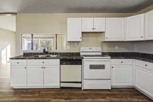 Kitchen featuring white appliances, white cabinets, dark countertops, and a textured ceiling