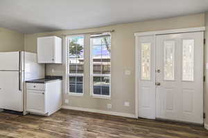 Kitchen with white cabinets, freestanding refrigerator, and dark wood-style flooring
