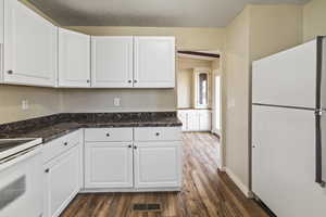 Kitchen with white appliances, white cabinets, dark wood-type flooring, dark stone counters, and a textured ceiling