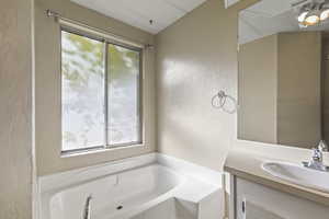 Bathroom with a textured wall, a bath, and vanity