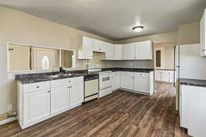 Kitchen featuring white cabinetry, dark wood-style floors, white appliances, dark countertops, and a textured ceiling