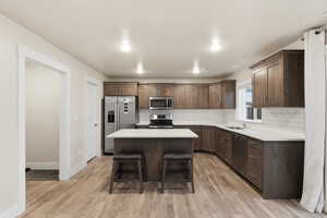 Kitchen featuring light wood-type flooring, appliances with stainless steel finishes, a breakfast bar area, dark brown cabinetry, and a center island
