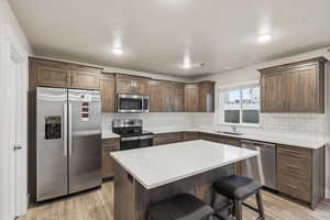 Kitchen featuring appliances with stainless steel finishes, a breakfast bar, a center island, and light wood-type flooring