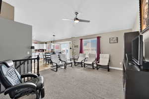 Living room featuring vaulted ceiling, carpet floors, and a ceiling fan