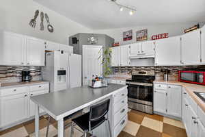 Kitchen with lofted ceiling, decorative backsplash, electric range, white cabinets,