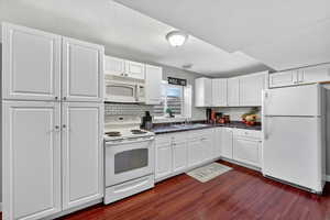 Kitchen featuring white appliances, white cabinets, and backsplash