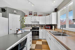 Kitchen with lofted ceiling, decorative backsplash, electric range, white cabinets,