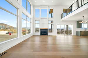 Unfurnished living room with a mountain view, a glass covered fireplace, light wood-style floors, recessed lighting, and a towering ceiling