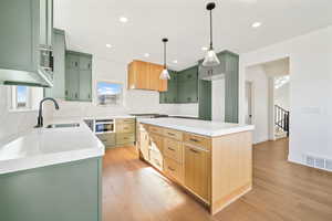 Kitchen featuring green cabinets, a kitchen island, light stone counters, light wood-type flooring, and tasteful backsplash