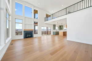 Unfurnished living room featuring a glass covered fireplace, a high ceiling, light wood-style floors, recessed lighting, and a chandelier