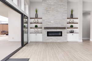 Unfurnished living room featuring light wood-style floors, a stone fireplace, and built in shelves