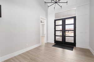 Entrance foyer with a chandelier, light wood-type flooring, a high ceiling, and french doors