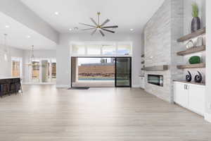 Living area featuring a stone fireplace, light wood-style floors, recessed lighting, a chandelier, and ceiling fan