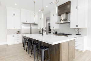 Kitchen with tasteful backsplash, an island with sink, white cabinets, a kitchen breakfast bar, and recessed lighting