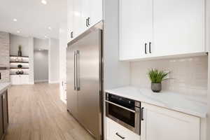 Kitchen with white cabinets, appliances with stainless steel finishes, recessed lighting, light wood finished floors, and light stone counters