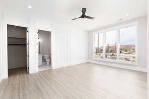 Unfurnished bedroom featuring a spacious closet, light wood-type flooring, a decorative wall, a ceiling fan, and recessed lighting