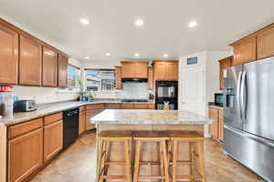 Kitchen with black appliances, recessed lighting, tasteful backsplash, a kitchen island, and brown cabinets