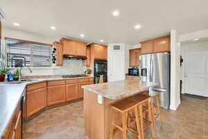 Kitchen featuring a kitchen breakfast bar, black appliances, backsplash, recessed lighting, and a center island