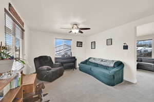 Carpeted living room featuring a ceiling fan and baseboards