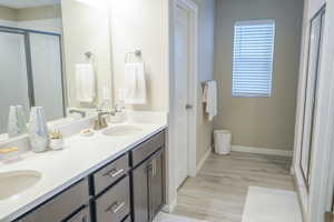 Full bathroom featuring a stall shower, double vanity, and light wood-style floors