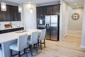 Kitchen featuring appliances with stainless steel finishes, dark brown cabinets, a kitchen bar, light wood finished floors, and recessed lighting