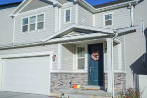 View of front facade featuring stone siding, a porch, an attached garage, and concrete driveway