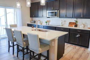 Kitchen with backsplash, a breakfast bar, stainless steel microwave, and light wood finished floors