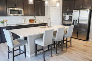 Kitchen featuring hanging light fixtures, stainless steel appliances, light wood-style flooring, dark brown cabinetry, and tasteful backsplash