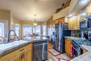 Kitchen with tile countertops, appliances with stainless steel finishes, a textured ceiling, light wood-style flooring, and pendant lighting