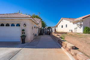 View of home's exterior with stucco siding, a tiled roof, concrete driveway, a patio, and a gate