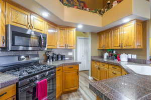 Kitchen featuring tile countertops, gas range, stainless steel microwave, light wood-type flooring, and brown cabinetry