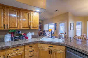 Kitchen with tile counters, dishwasher, brown cabinetry, a peninsula, and a textured ceiling